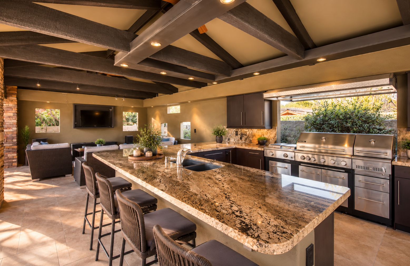 Covered outdoor kitchen with a stone island, beamed ceiling and lounge seating at Oasis